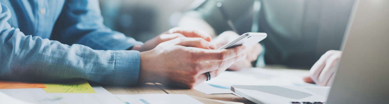 Mann sitzt mit Handy vorm Laptop