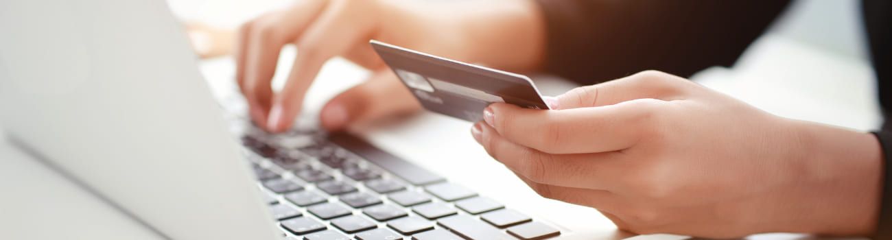 Frau sitzt am Laptop mit einer EC Karte in der Hand