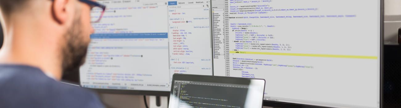 Mann sitzt vor zwei Monitoren und sieht sich den Quellcode an.