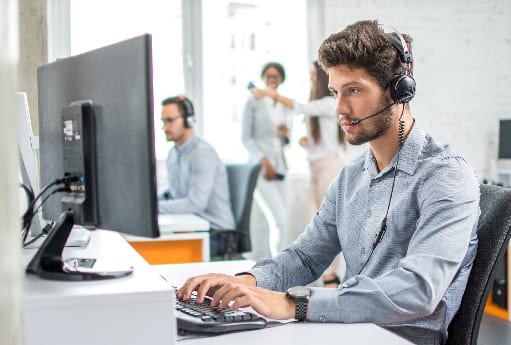 Mann sitzt am Rechner mit Headset auf dem Kopf.